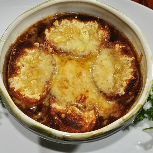 bowl of French onion soup with parsley garnish on a porcelain plate